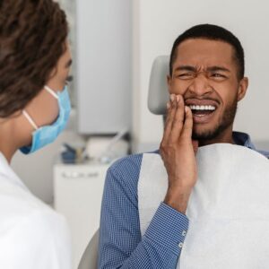 Persona sosteniendo su mandíbula debido a dolor dental, recibiendo atención de urgencia.