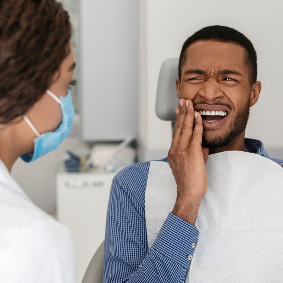Persona sosteniendo su mandíbula debido a dolor dental, recibiendo atención de urgencia.